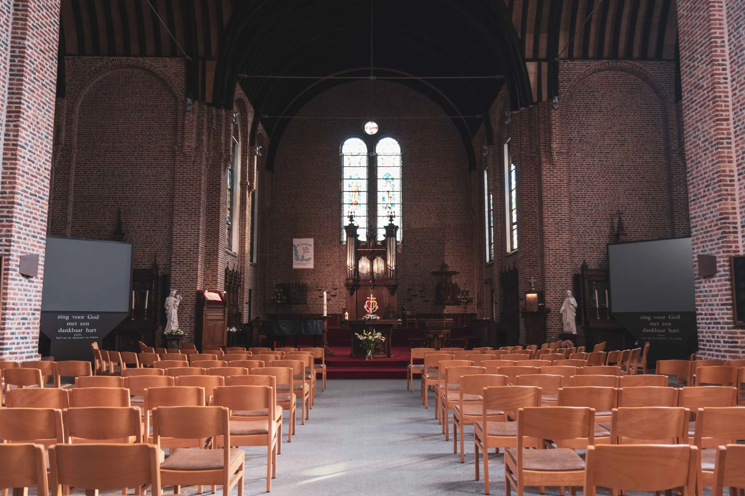Interieur van een kerk met rijen houten stoelen, een altaar, religieuze iconen, en kleurrijke glas-in-loodramen.