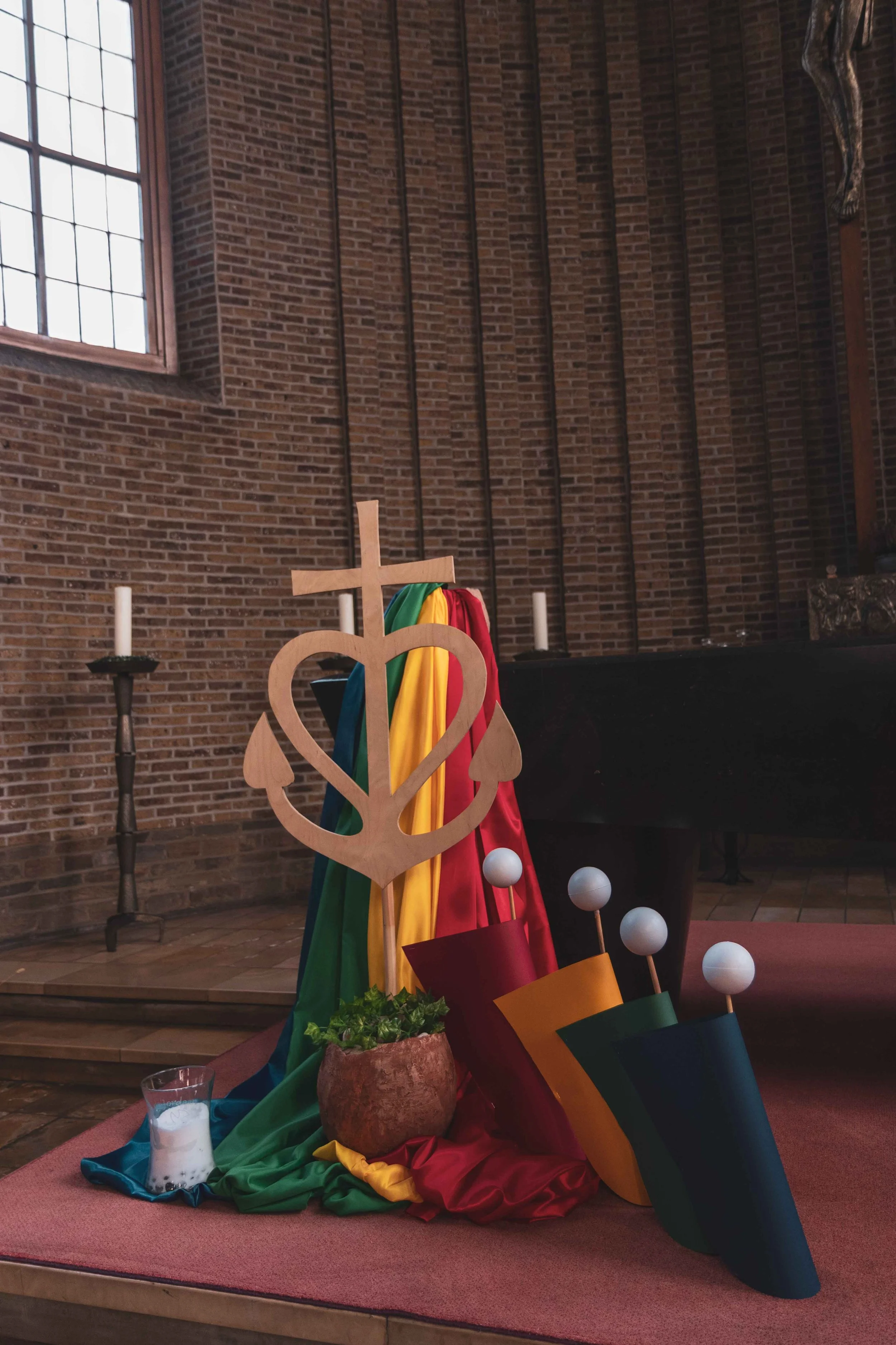 Kerkinterieur met kleurrijke decoratie, waaronder een houten symbolisch object, kaarsen, en kleurrijke stoffen en kersenkopjes, voor een religieuze of feestelijke ceremonie.
