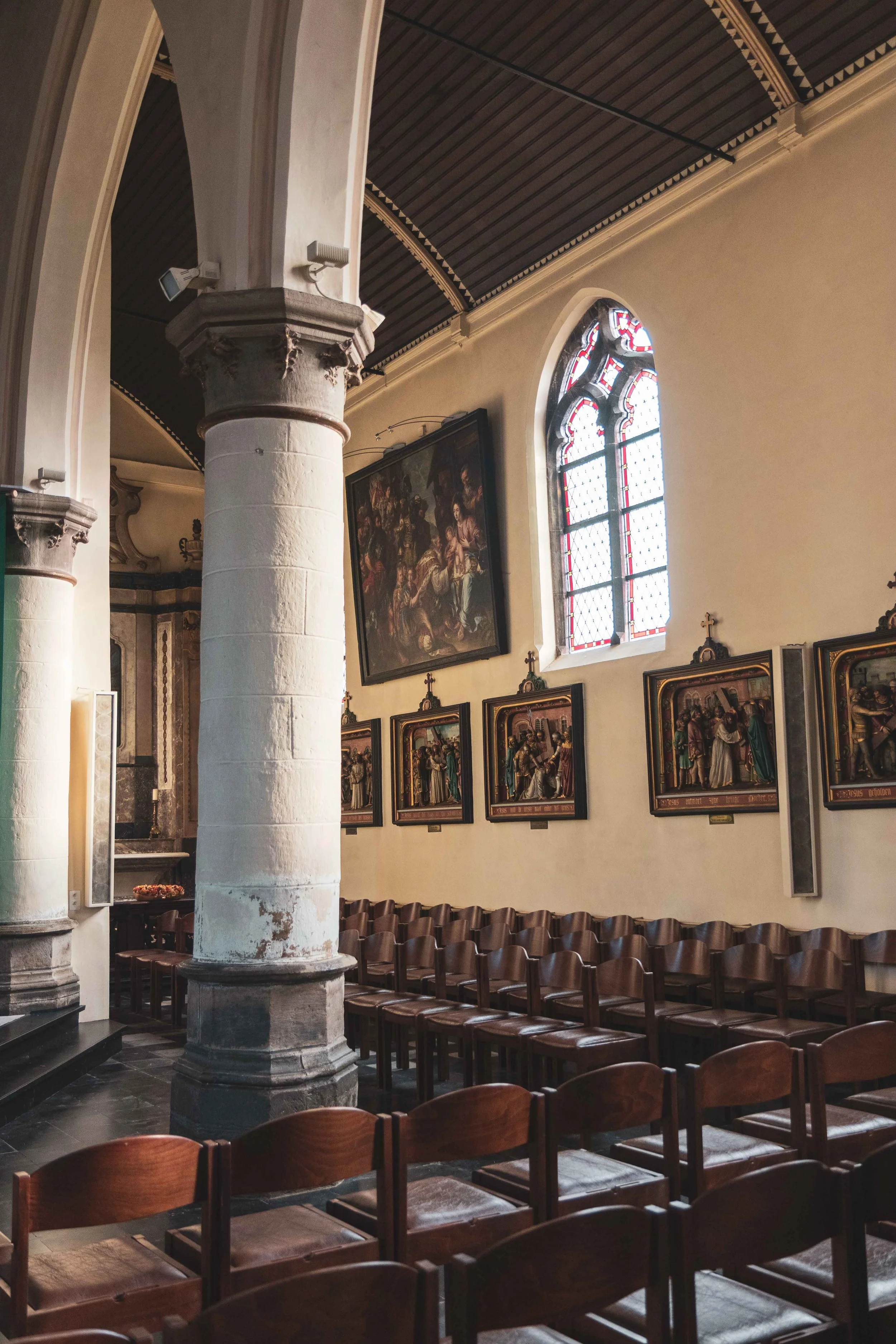 Interieur van een kerk met houten banken, schilderijen en een raam met gekleurnd glas