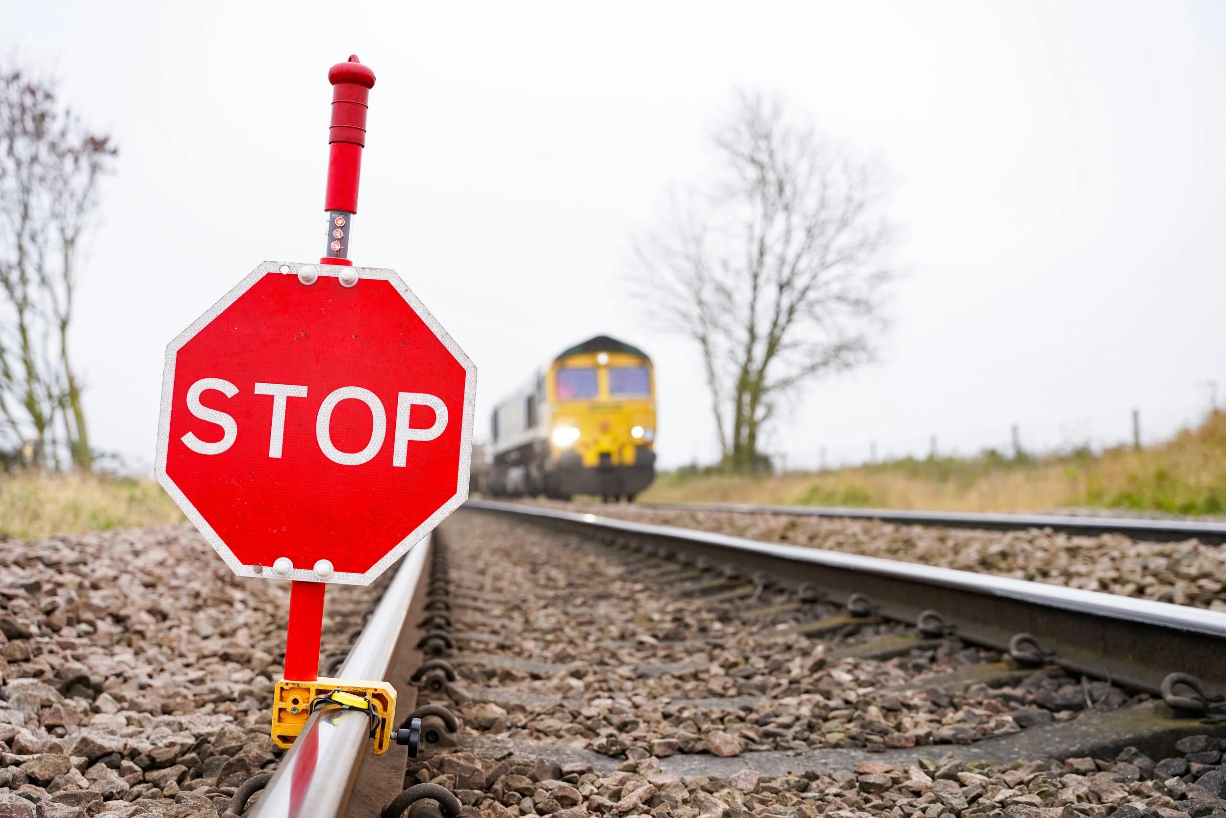 A stop sign mounted on a railroad track with a train approaching in the background.