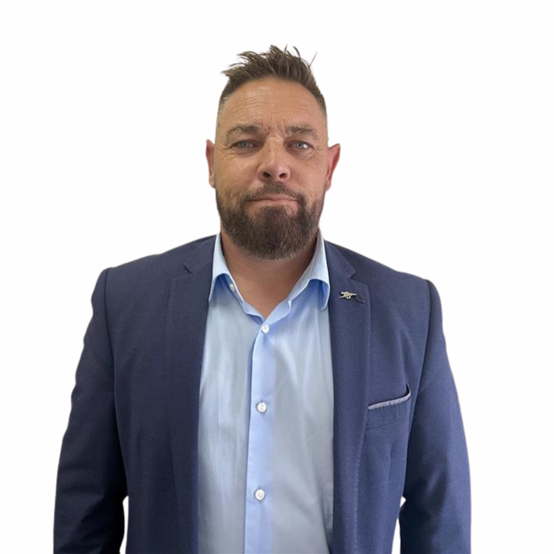 A man with a beard and styled hair wearing a blue blazer over a light blue dress shirt, standing against a white background.