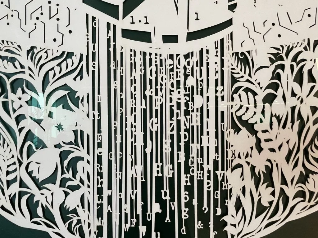 Intricate white paper cutout with botanical and musical motifs surrounding a central musical notes chart.