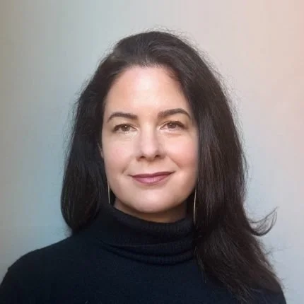 Portrait of a woman with long dark hair wearing a black turtleneck against a plain background.