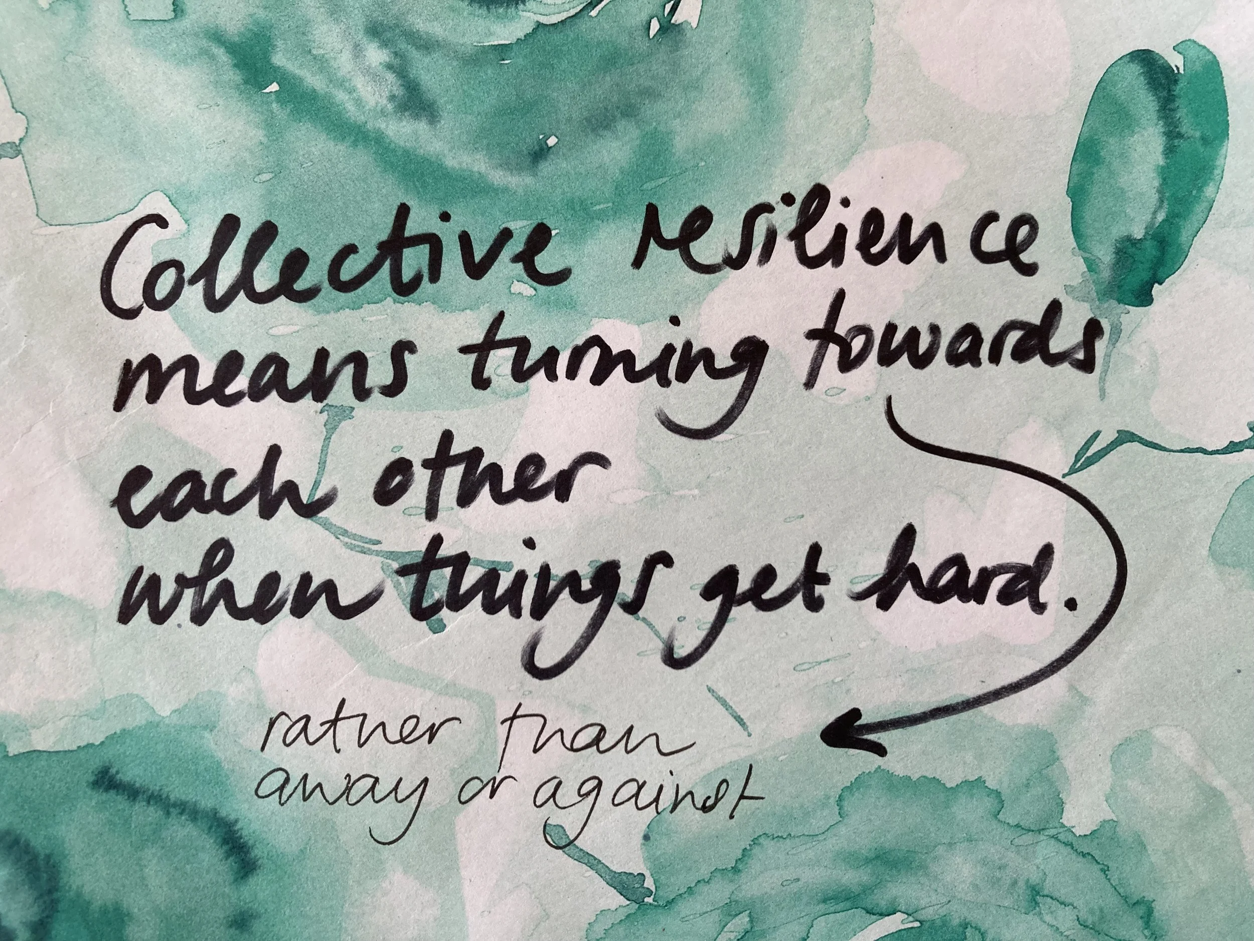 The sentence ‘Collective resilience means turning towards (rather than away or against) each other when things get hard’ is handwritten in black font on a white piece of paper with shapes in turquoise watercolour.