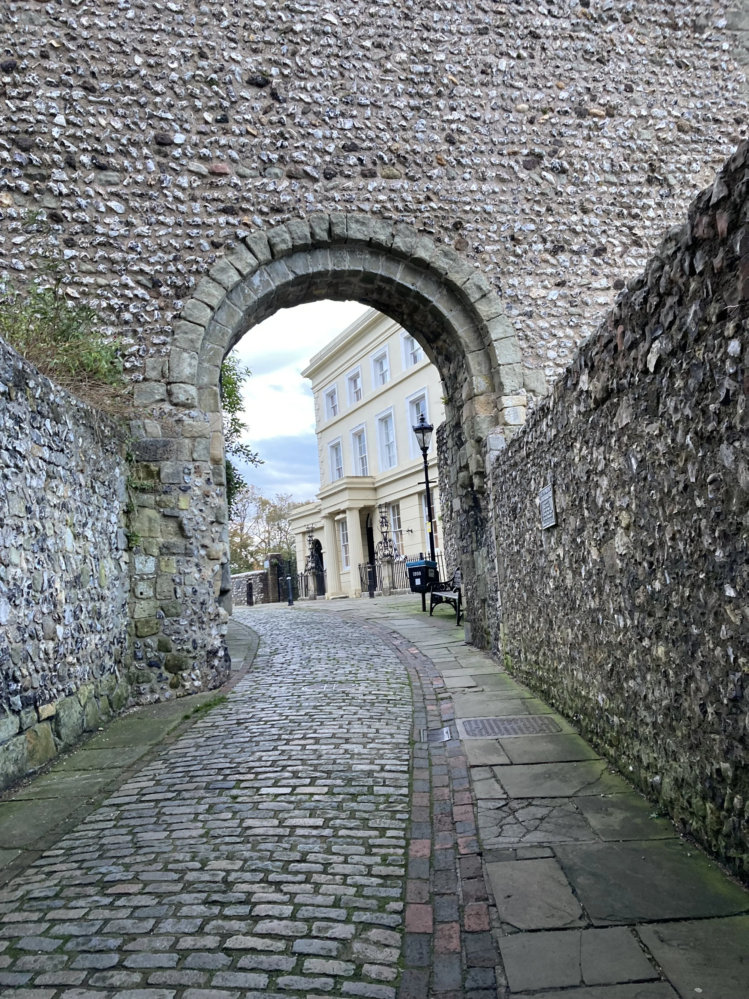 Photograph of an arch made of stone above a cobbled street with some blue sky visible in the background