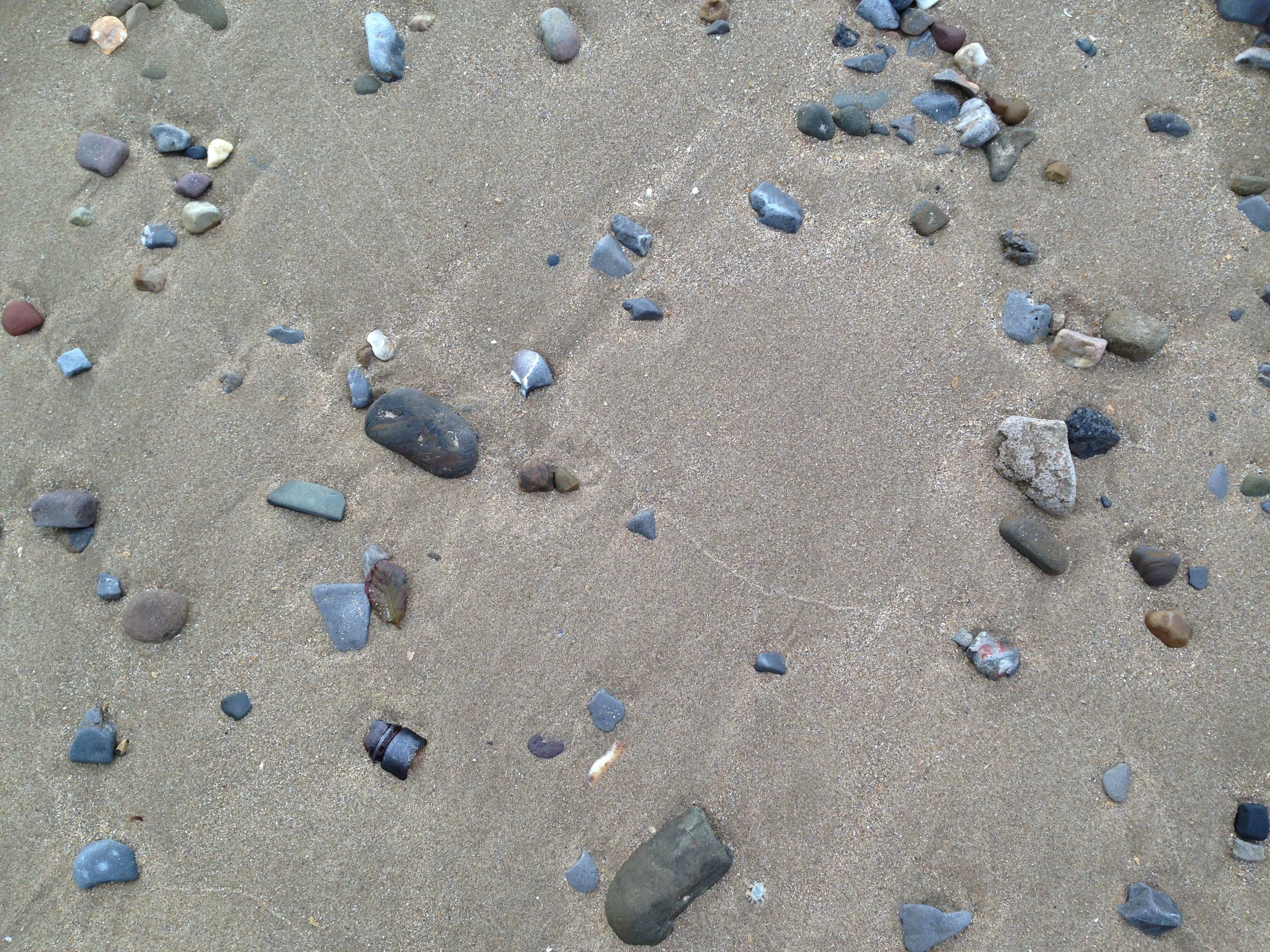 Close up photograph of pebbles of different colours and sizes scattered on a sandy beach