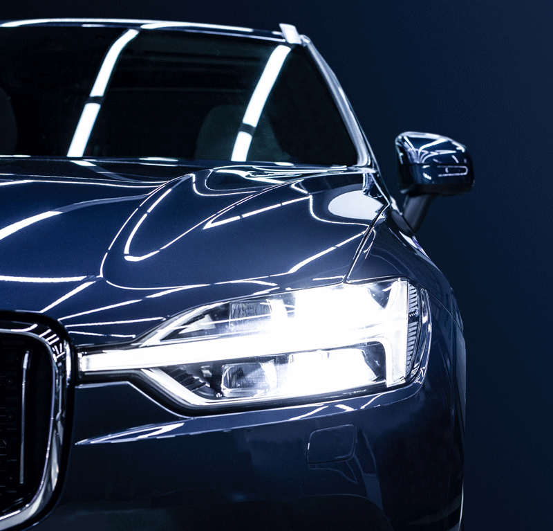 Close-up of a sleek black luxury car with reflective surface and LED headlights, against a dark background.