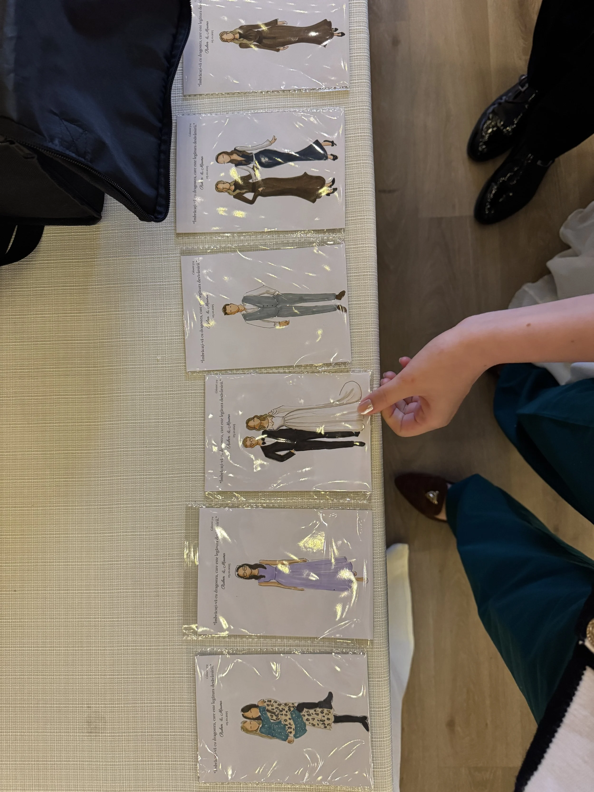 A person pointing at a fashion illustration card on a table among five other cards, each featuring a different stylish outfit worn by a female model.