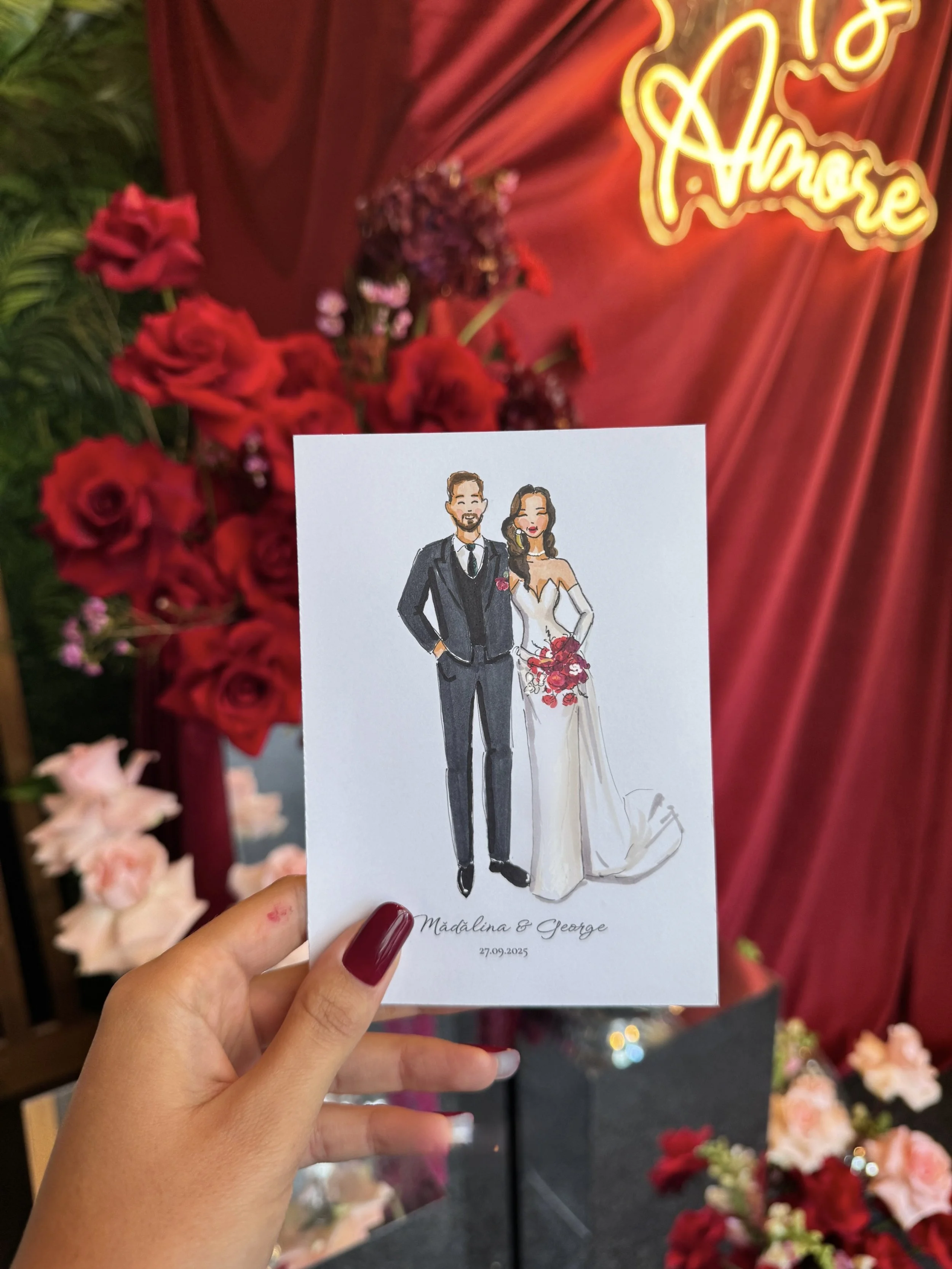 A hand holding a wedding guest sketch illustration of a bride and groom in front of a flower arrangement with red roses and a neon sign that says 'A Love To Remember'.