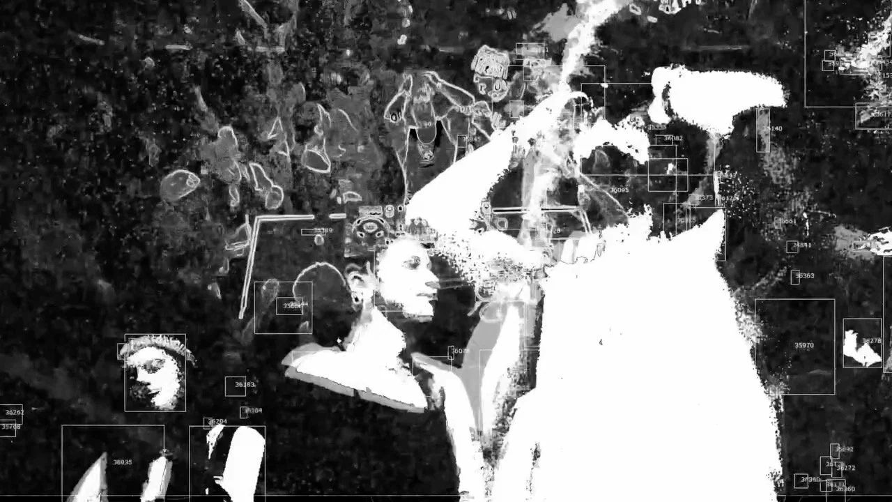 Image en noir et blanc d'une personne avec un casque de réalité virtuelle, entourée de plusieurs autres figures humaines, avec des annotations de reconnaissance faciale.