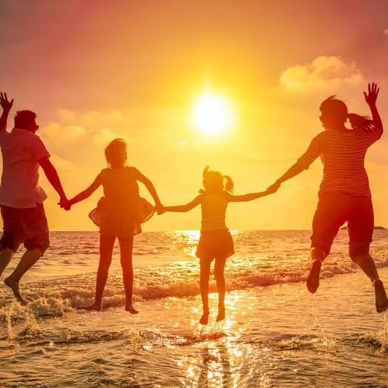 Four people holding hands and jumping in the water at sunset on the beach.