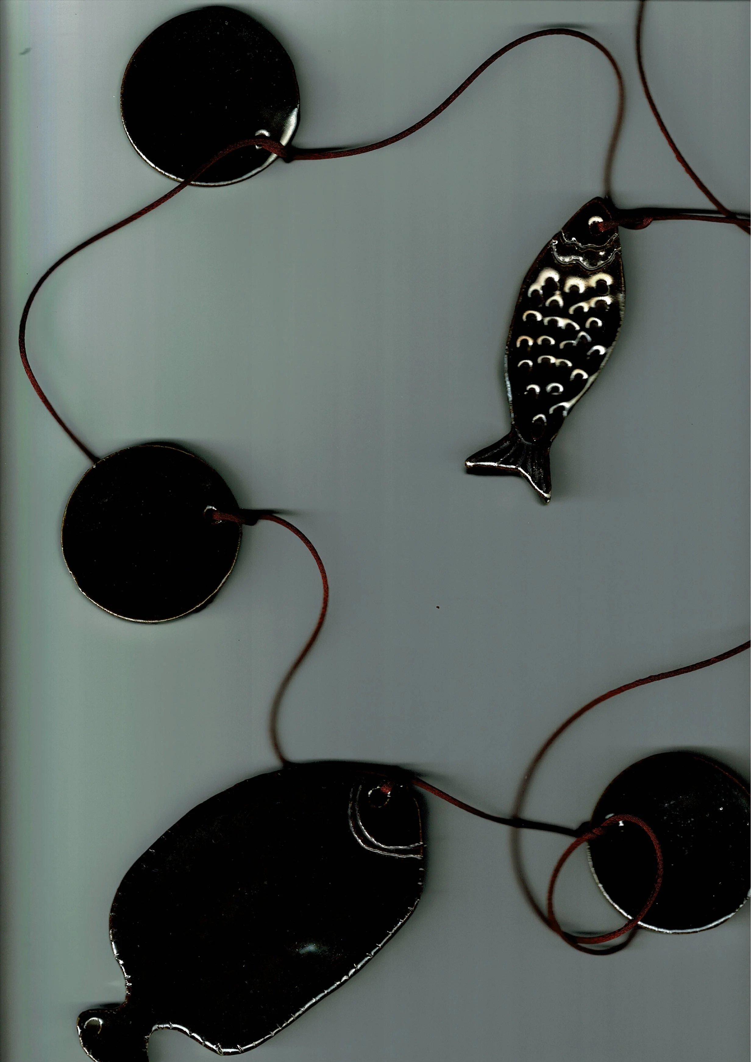 Un collier avec des pendentifs en forme de rond, d'un poisson en métal et de formes abstraites, avec des cordons en fil rouge.