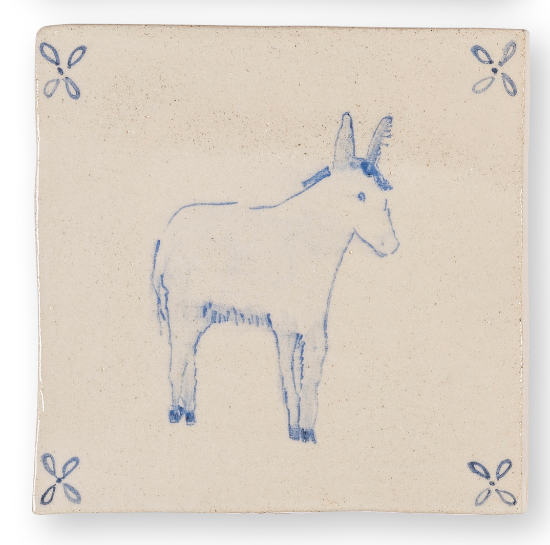 Une assiette en céramique beige avec une simple illustration bleue d'une licorne au centre, et des décorations florales bleues aux coins.
