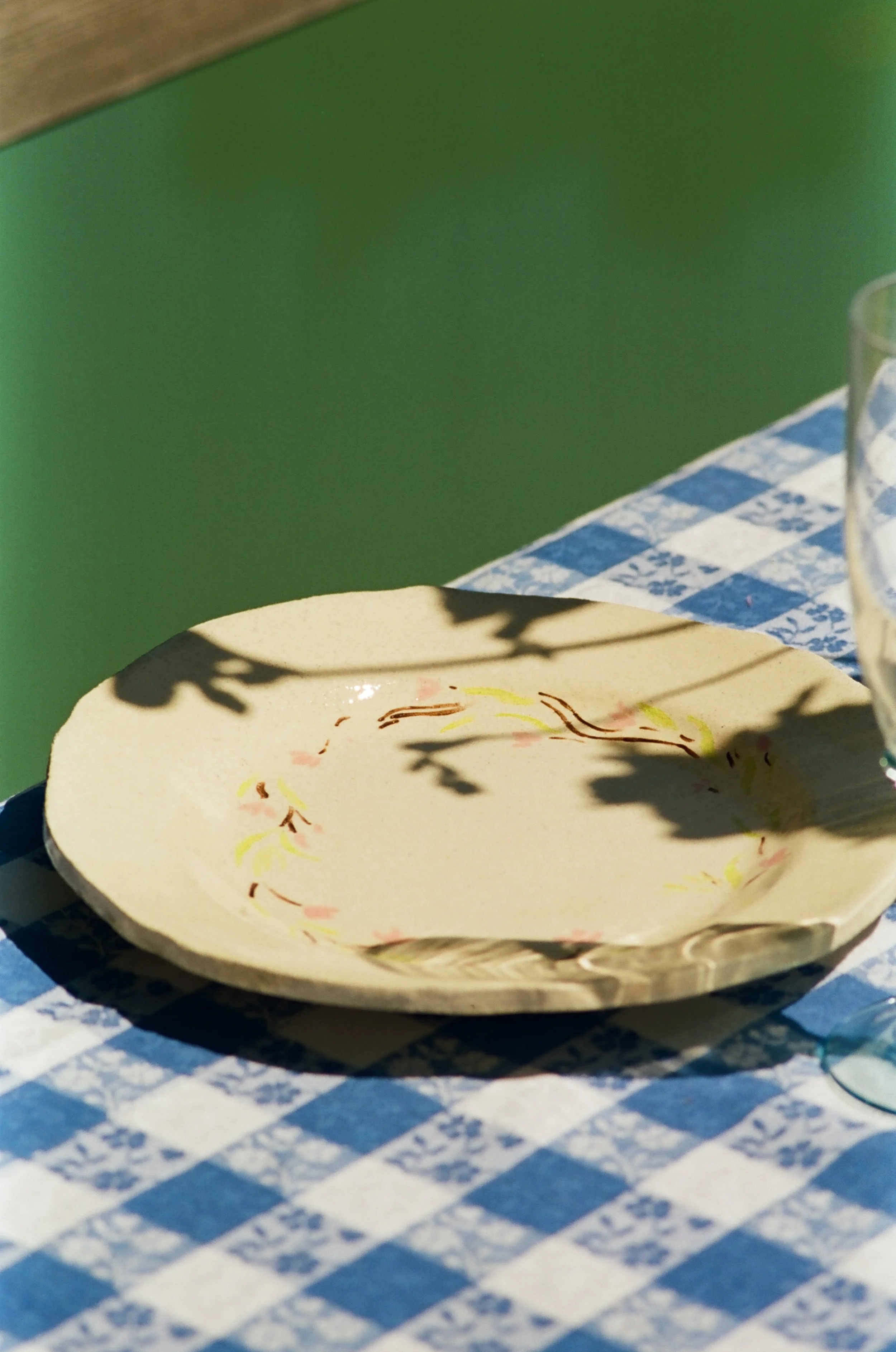 Assiette en céramique beige avec des motifs colorés, posée sur une nappe à carreaux bleus et blancs, avec un verre en partie visible à côté.