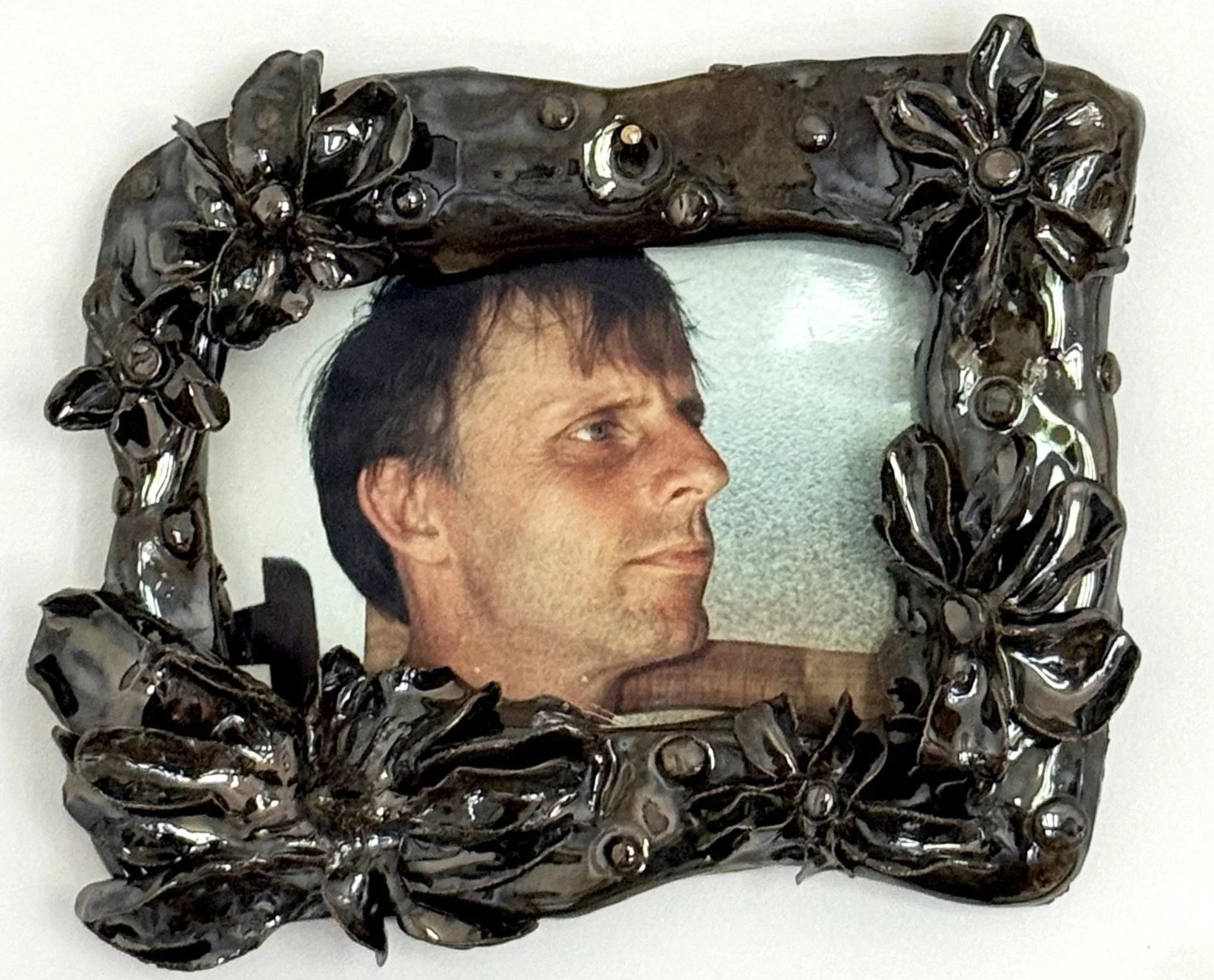 Un miroir au cadre en bois sculpté de fleurs et de feuilles, reflétant le visage d'un homme avec des cheveux bruns courts.