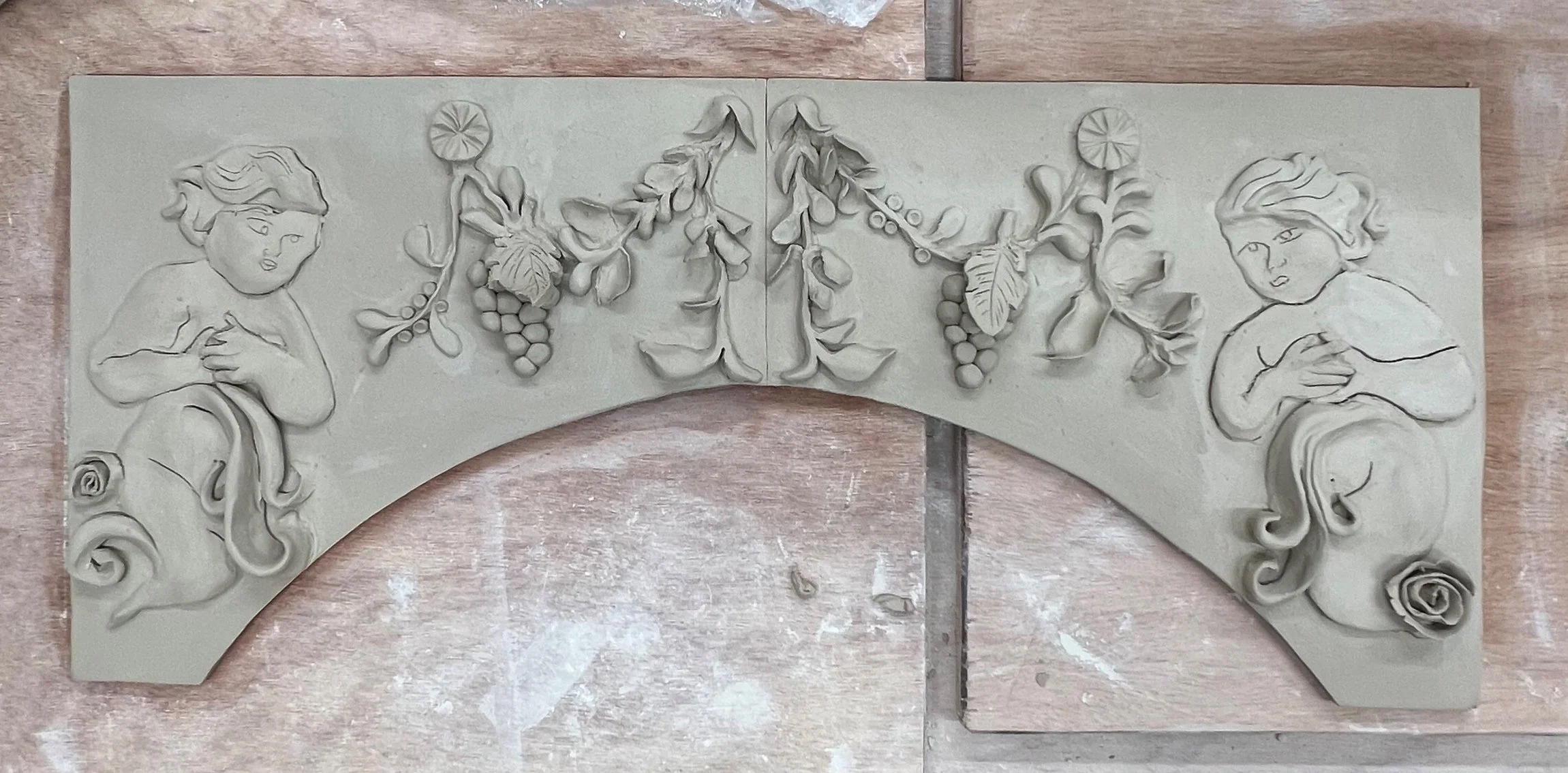 Une plaque en relief en forme de demi-cercle représentant deux figures de jeunes enfants et des branches de raisin avec des feuilles et des grappes. Les enfants sont dessinés avec des expressions curieuses et tiennent leur poitrine.