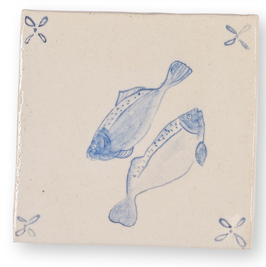 Carreau de céramique avec une illustration bleue de deux poissons et quatre motifs floraux dans les coins.