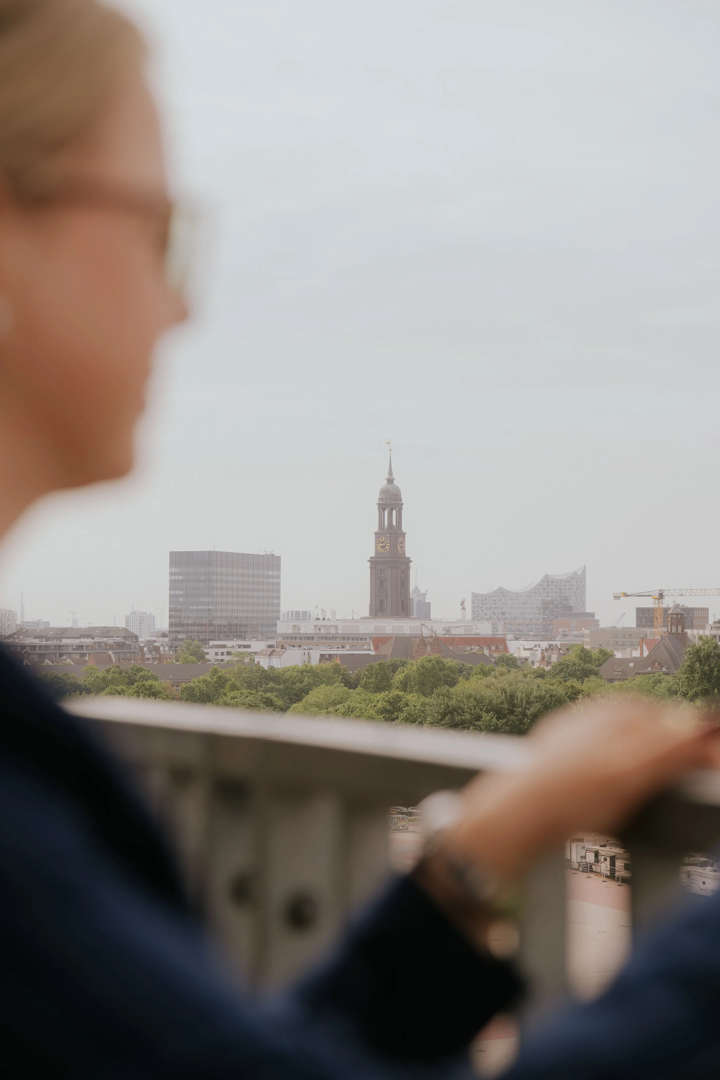 Eine Frau blickt auf die Skyline von Hamburg, mit der Kirche St. Michaelis im Hintergrund