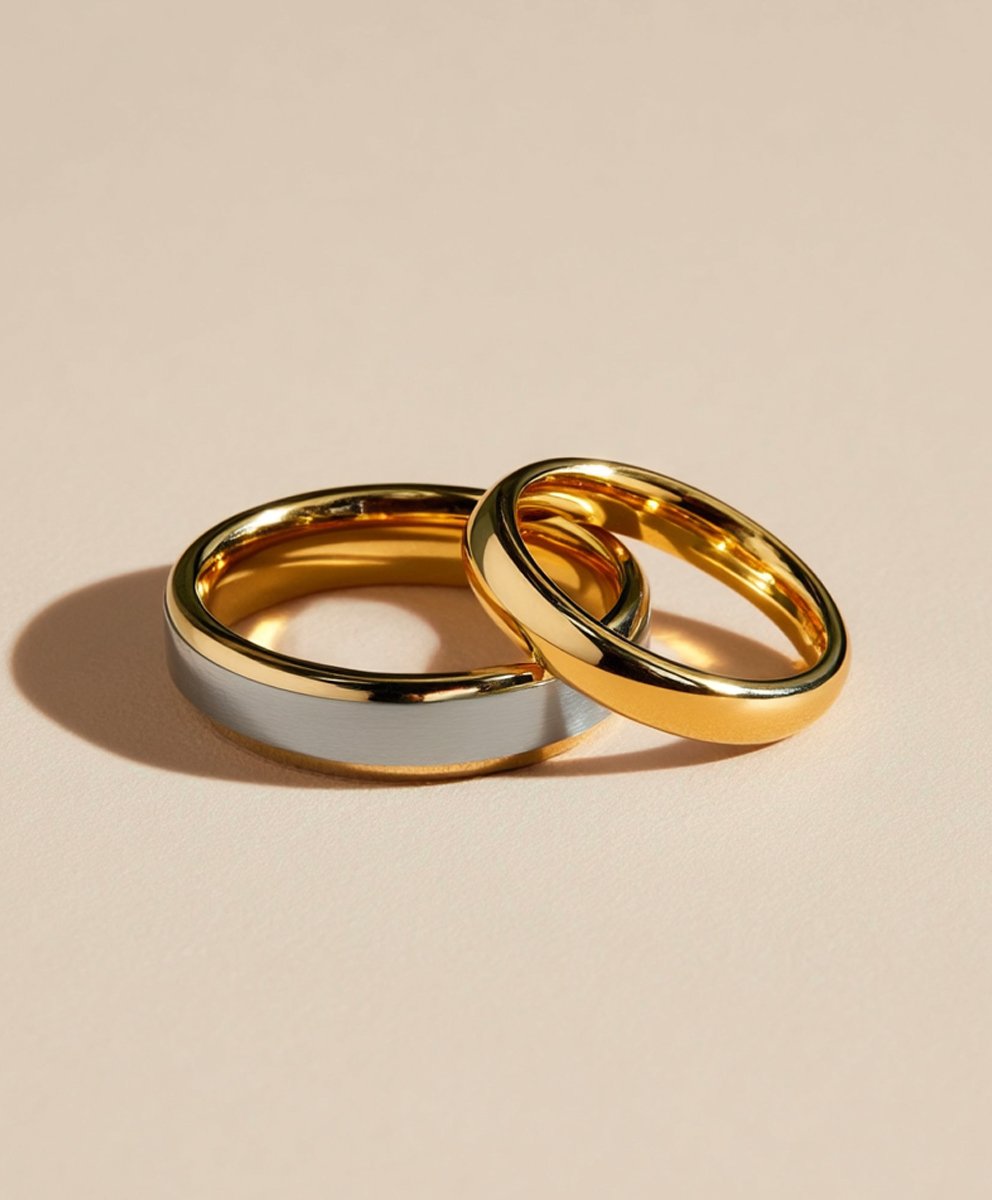 Two wedding rings, one gold and one silver, placed on a light-colored surface, casting shadows.