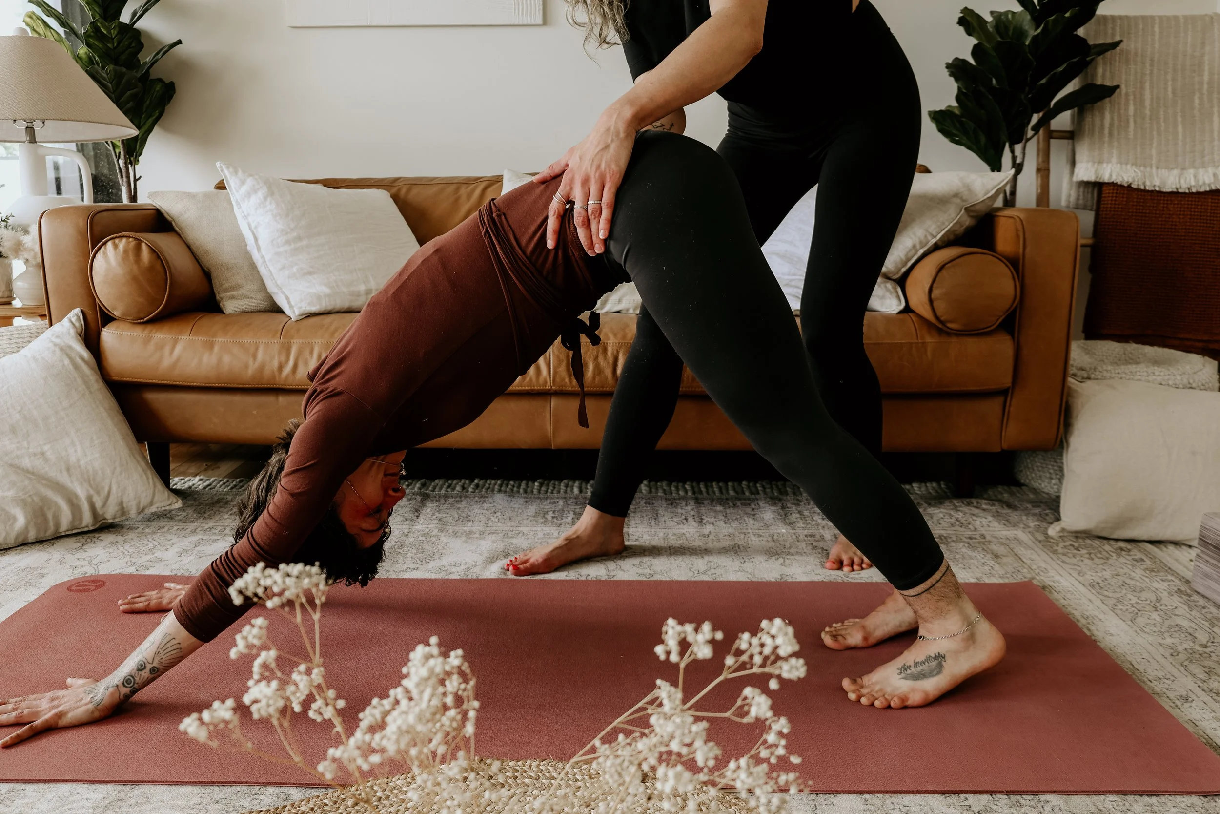 Yoga therapy session in a living room, the client in downward dog pose and the yoga therapist adjusting the clients stance.
