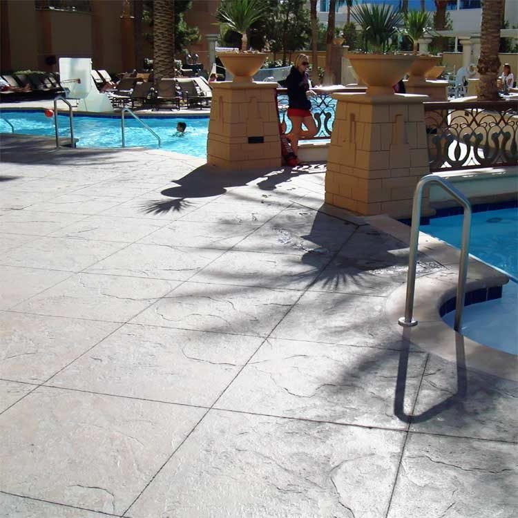 Hotel swimming pool area with lounge chairs, palm trees and guests relaxing on a coated pool deck.