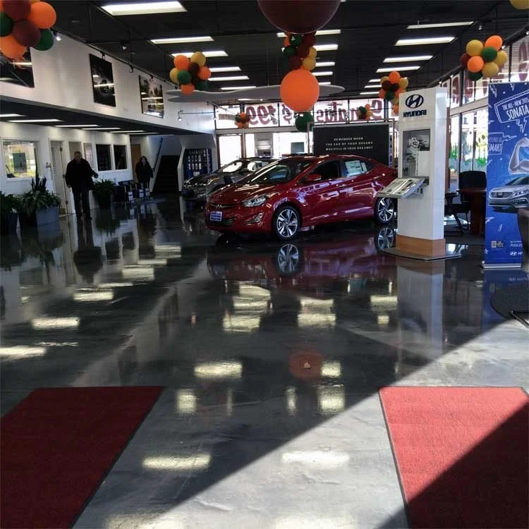Car dealership showroom with three cars on display under balloons on a shiny reflective metallic floor.