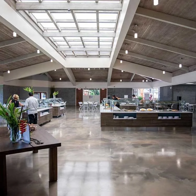 Spacious school cafeteria with buffet stations and white chairs under a large skylight ceiling.
