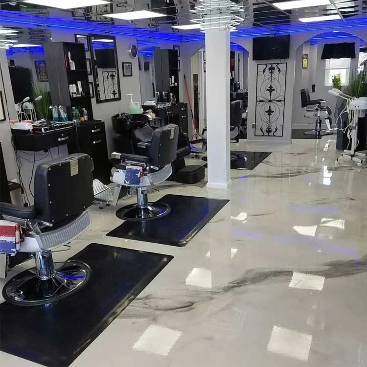 Modern barbershop interior with black chairs and mirrors, lit by blue LED lighting above a self-leveling floor.