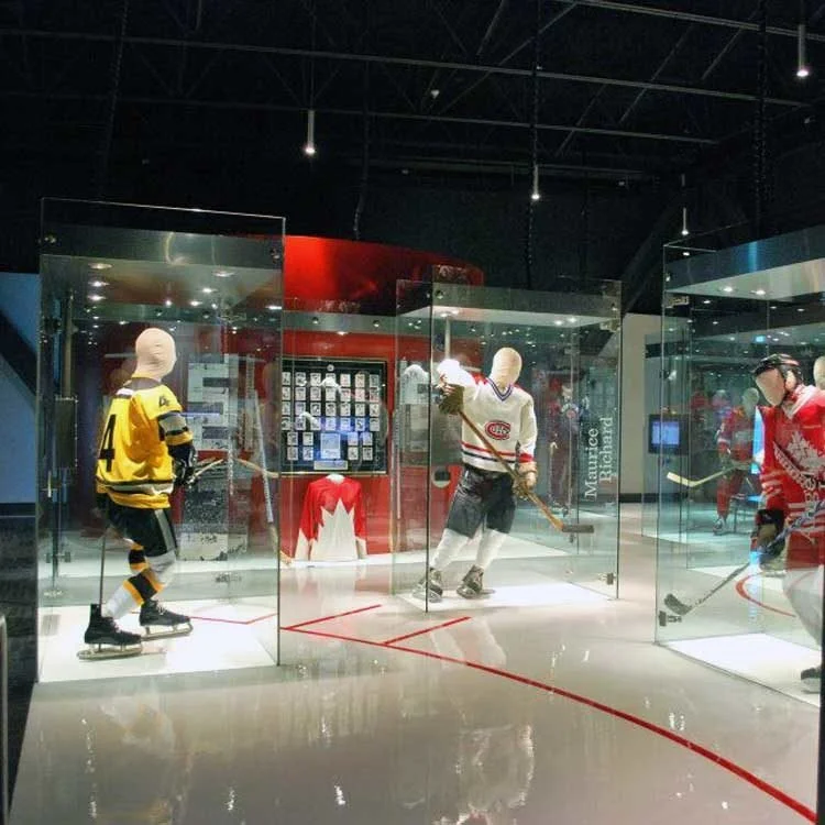 Museum exhibit of hockey mannequins in jerseys inside a glass display case on a coated floor.