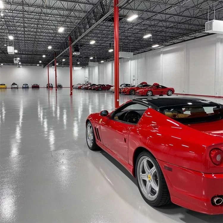 Red sports car parked in a large showroom with other sports cars in the background on a glossy coated floor.