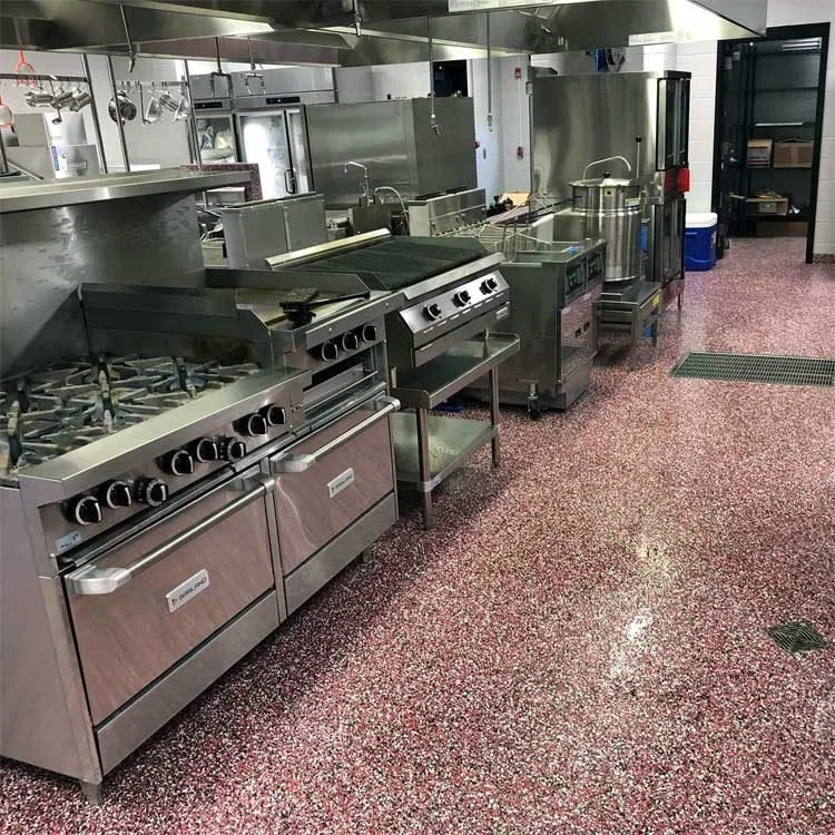 Commercial kitchen with stainless steel stoves and ovens on a red speckled flake epoxy floor.