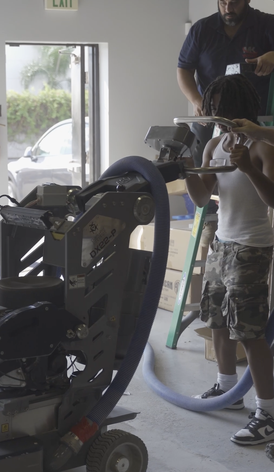 Family-owned epoxy business: A young boy learning the trade by operating a concrete grinder during a hands-on epoxy class and training session with professional supervision.