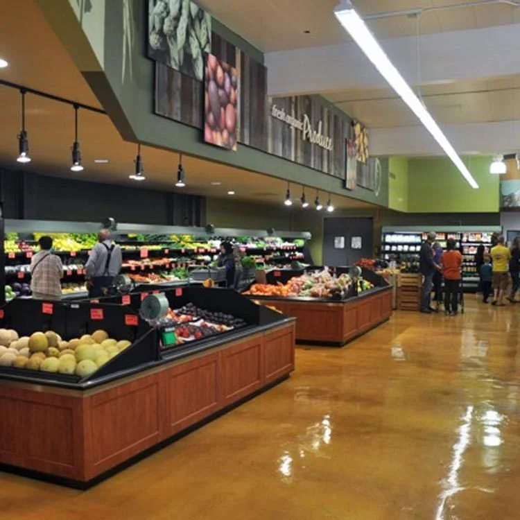 Grocery store produce section with fruit and vegetable displays and customers shopping on a coated floor.