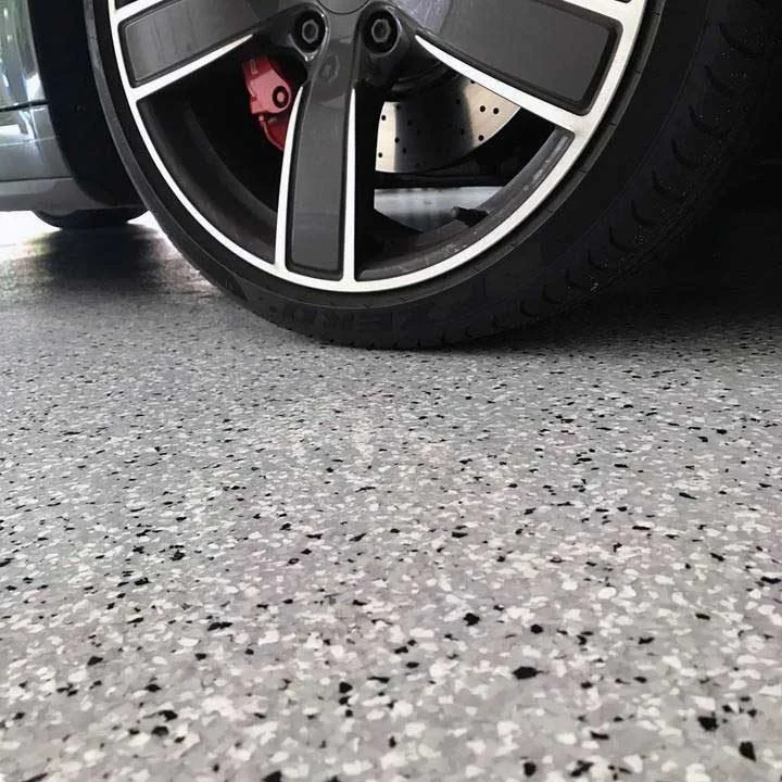 Close-up of a car wheel and brake caliper parked on a speckled flake epoxy garage floor.