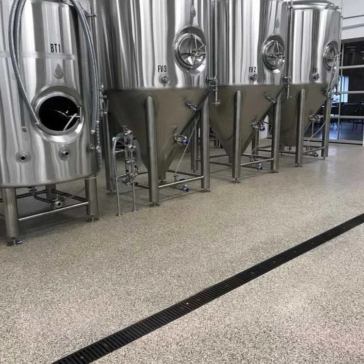 Three large stainless steel fermentation tanks lined up in a brewery on a speckled gray flake floor.