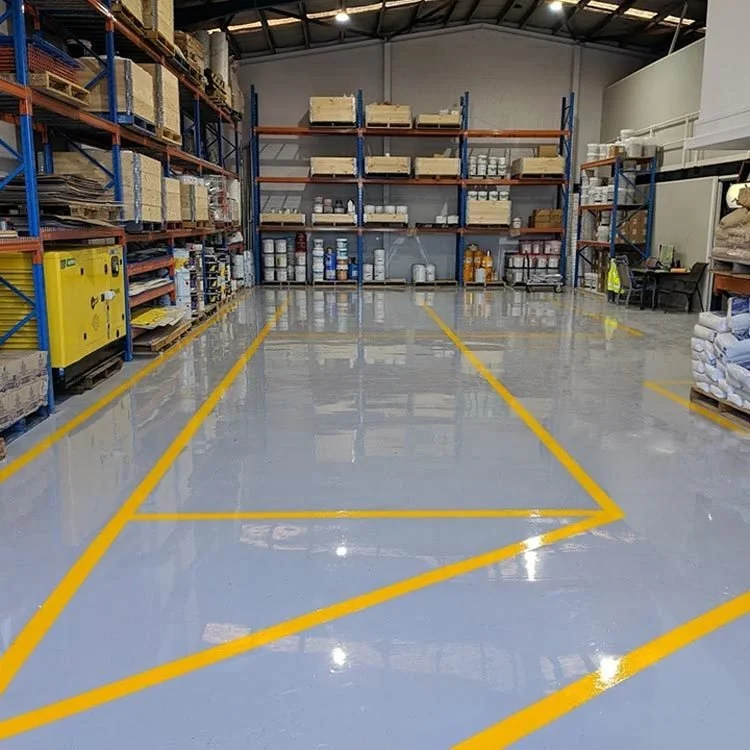 Empty warehouse with yellow line markings on a shiny, reflective epoxy-coated concrete floor and stocked metal shelving in the background.
