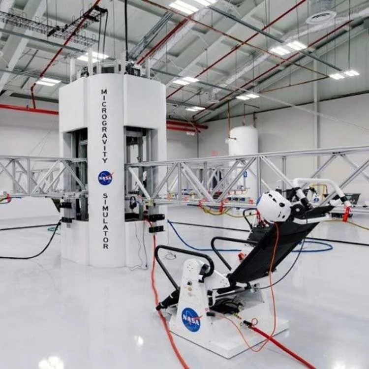 NASA microgravity simulator with equipment and harnesses in a white-walled laboratory with a seamless resinous floor.