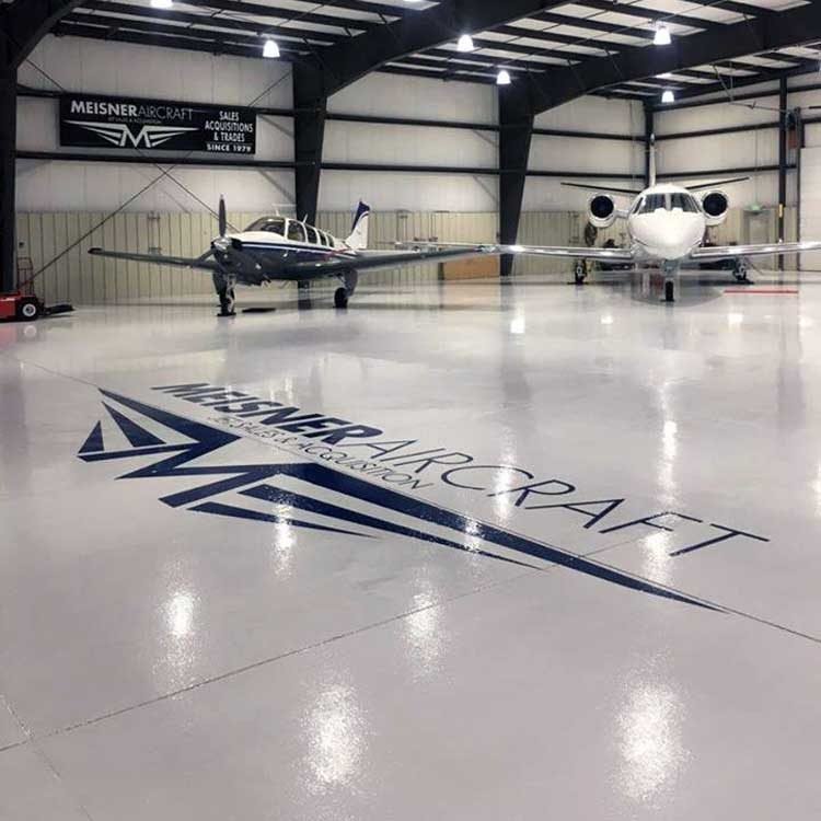 Two private jets inside a spacious aircraft hangar with a high-gloss white floor and an embedded company logo.