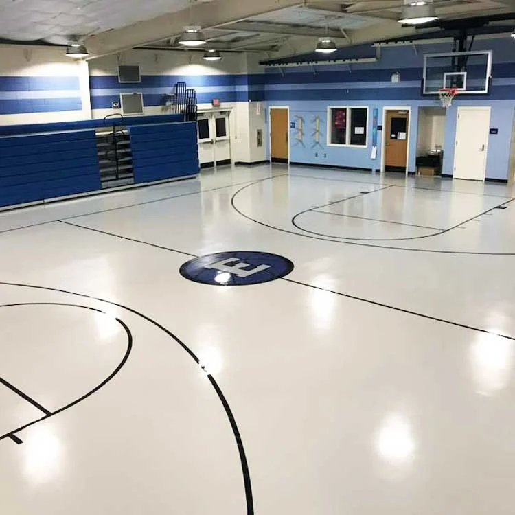 Indoor basketball gym with a polished coated court floor, black court lines and a center logo.