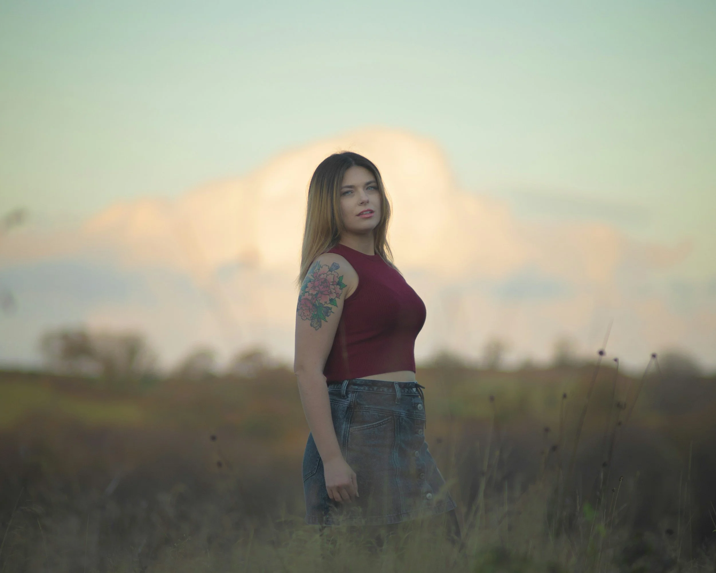 woman stands on florida beach. she is wearing a crop top and jeans and has a floral tattoo on her arm
