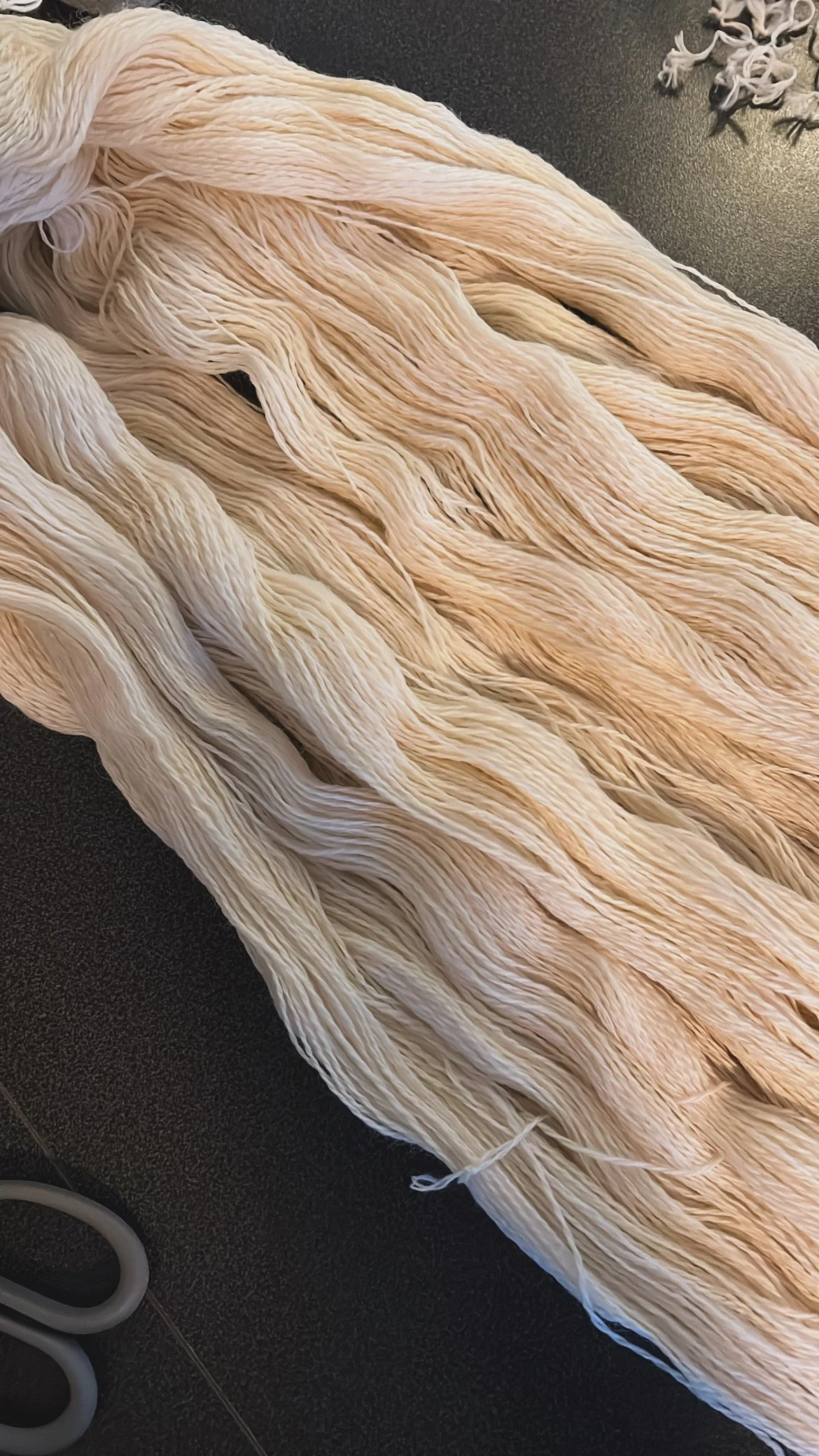 Close-up of bundles of raw, light-colored yarn, on a dark surface.