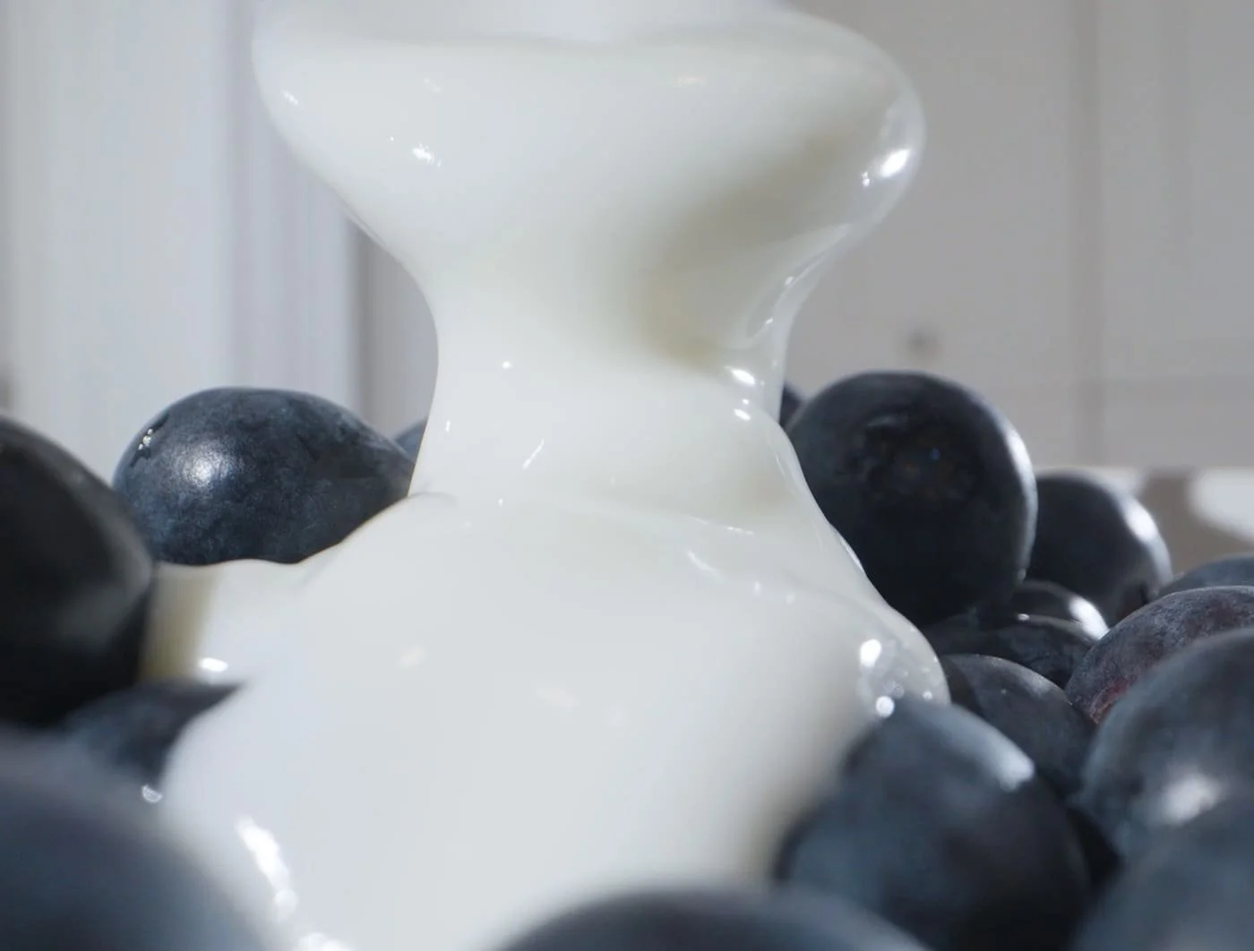 Close-up of blueberries with white creamy substance pouring over them.