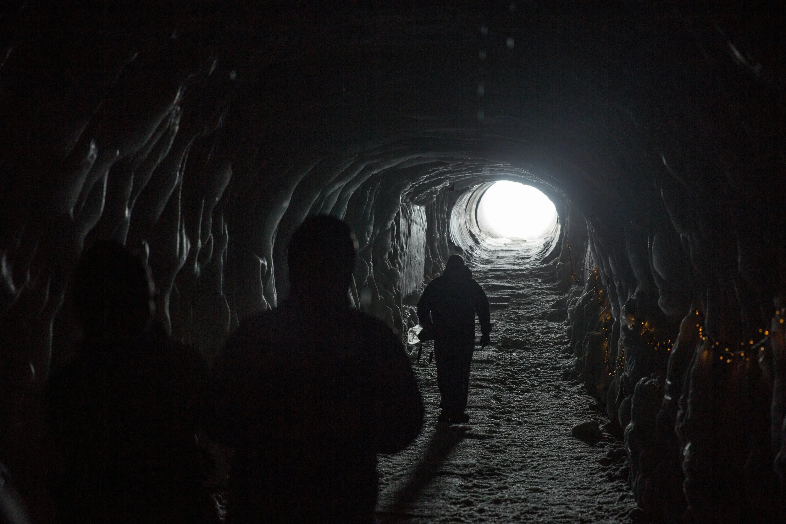 People walking inside a snow tunnel towards light at the exit.