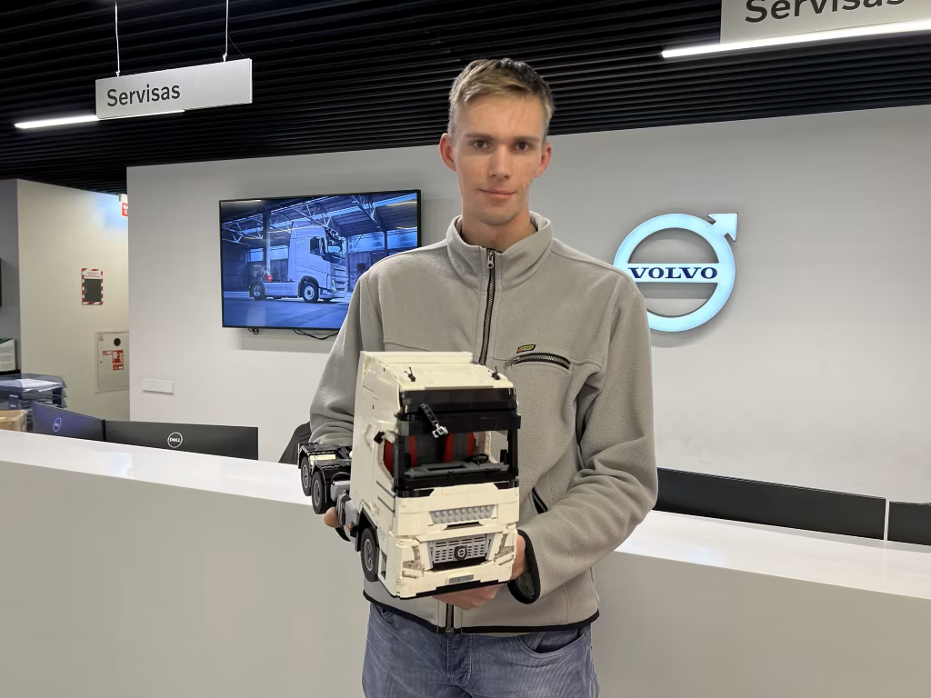 A young man holding a LEGO model of a semi-truck inside a Volvo dealership.