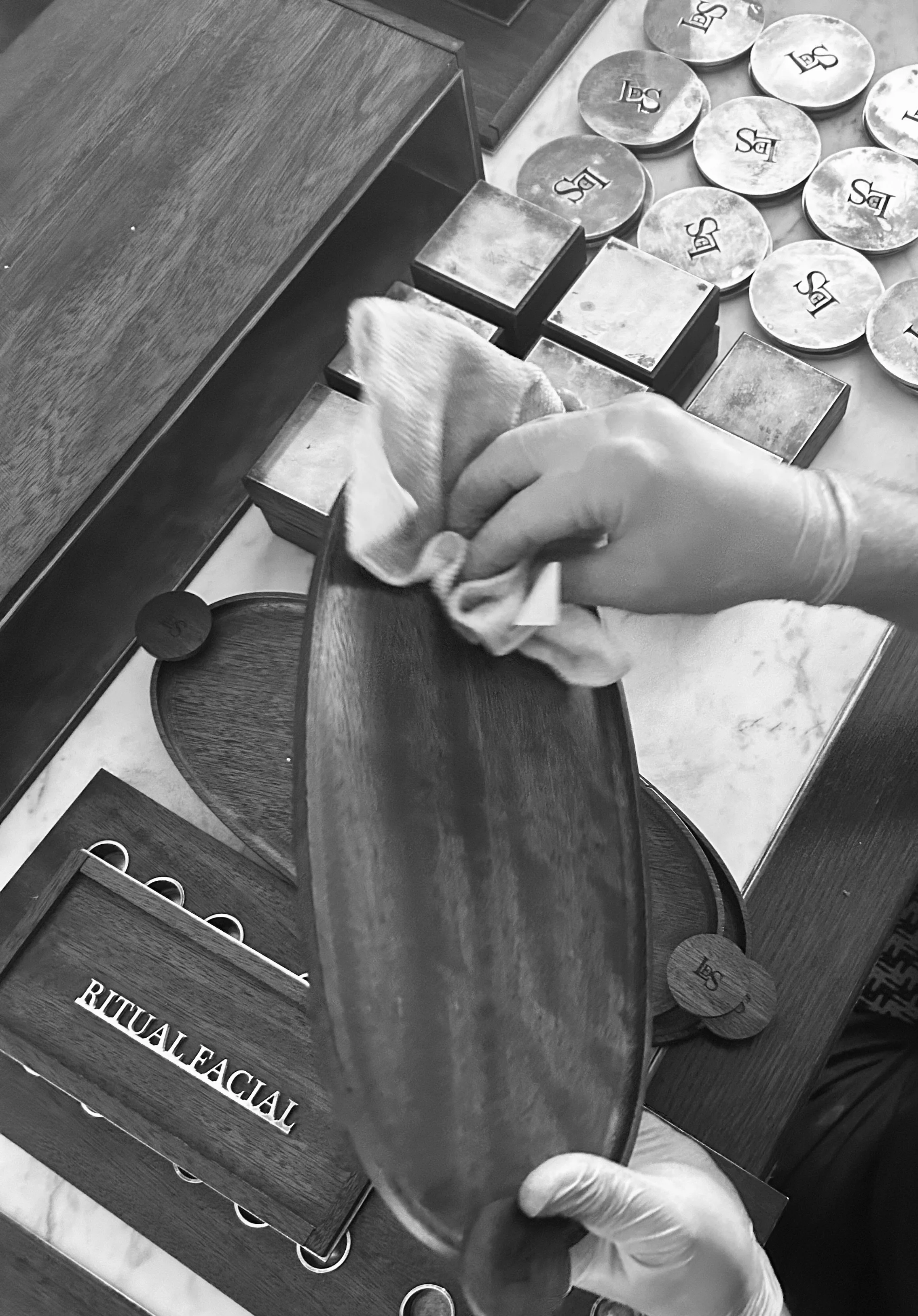 Person polishing some handmade props with skincare jars and boxes labeled 'RITUAL FACIAL' on the table.