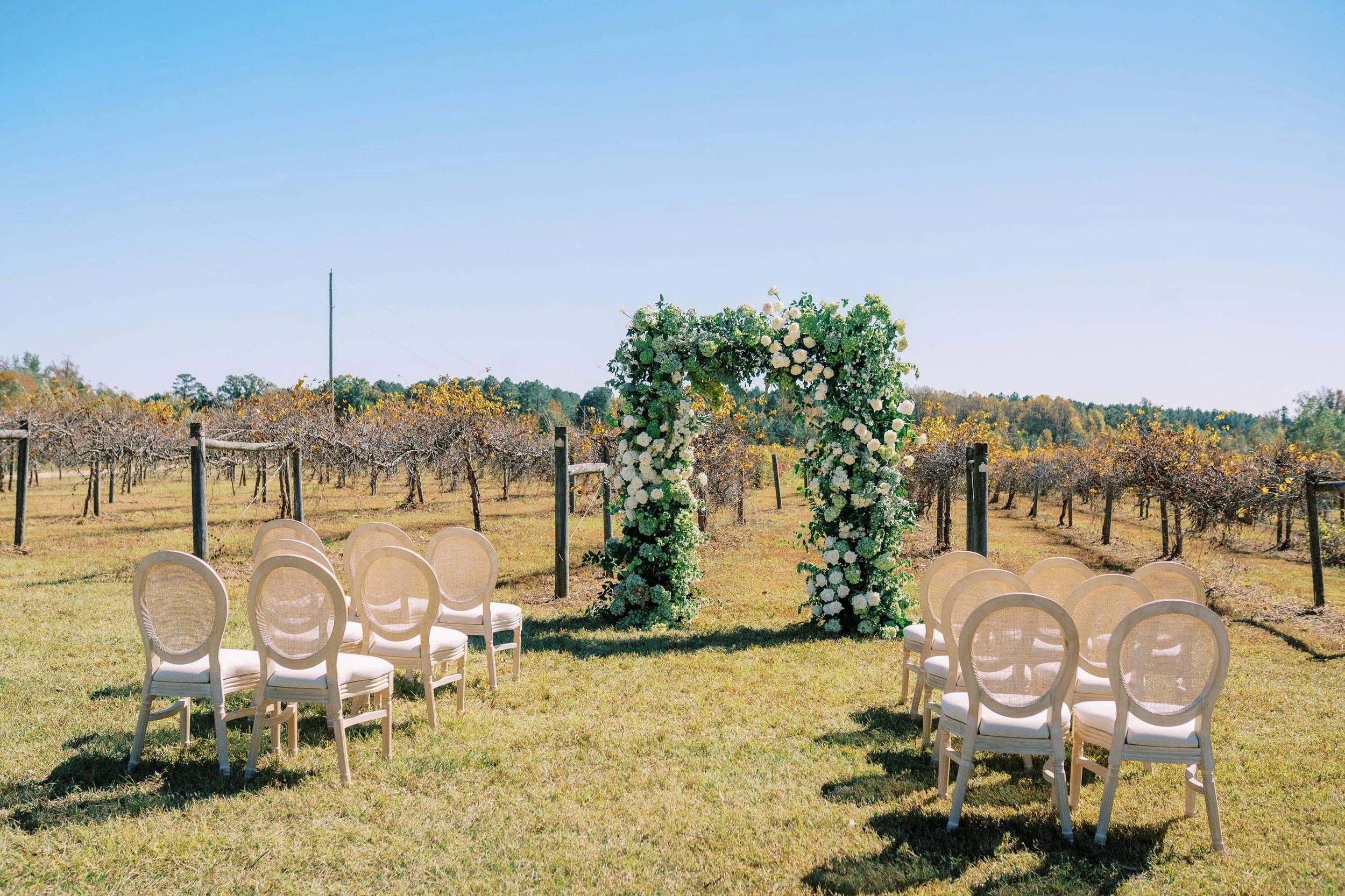 wedding ceremony setup with floral arch and Louis Chairs