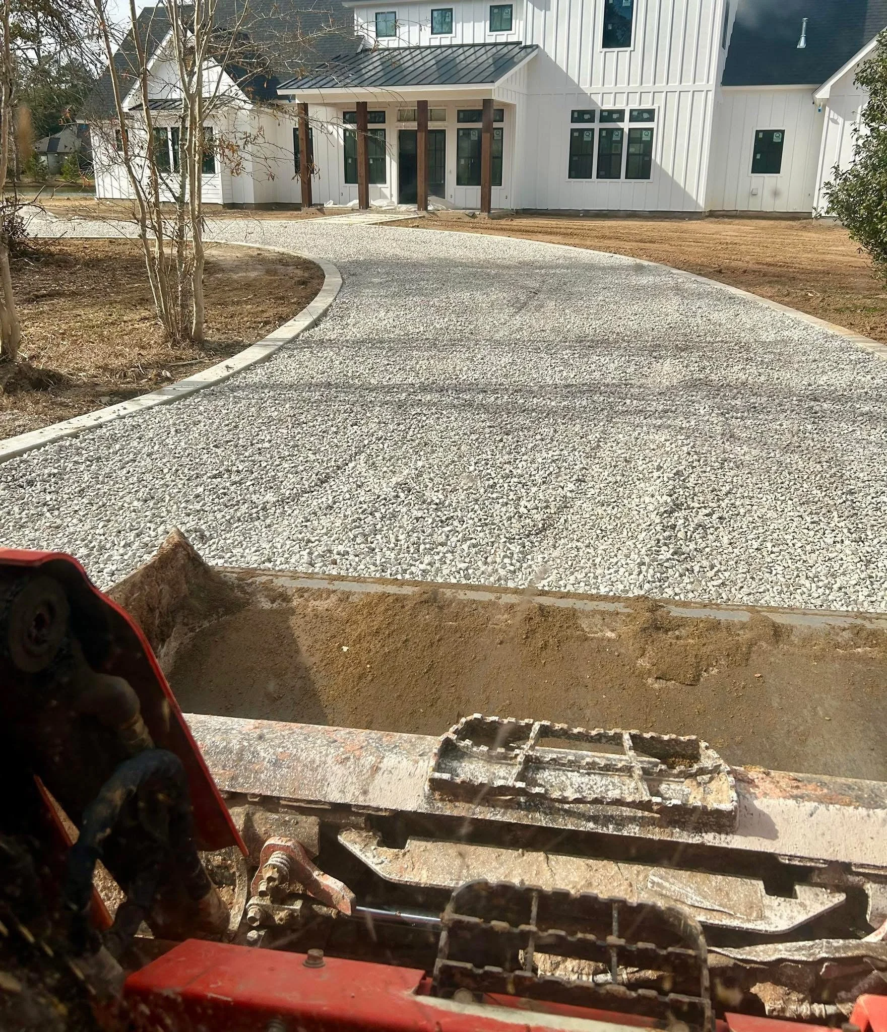 A gravel driveway in front of a garage with a closed white door, a gray wall, and wooden fences on the sides.