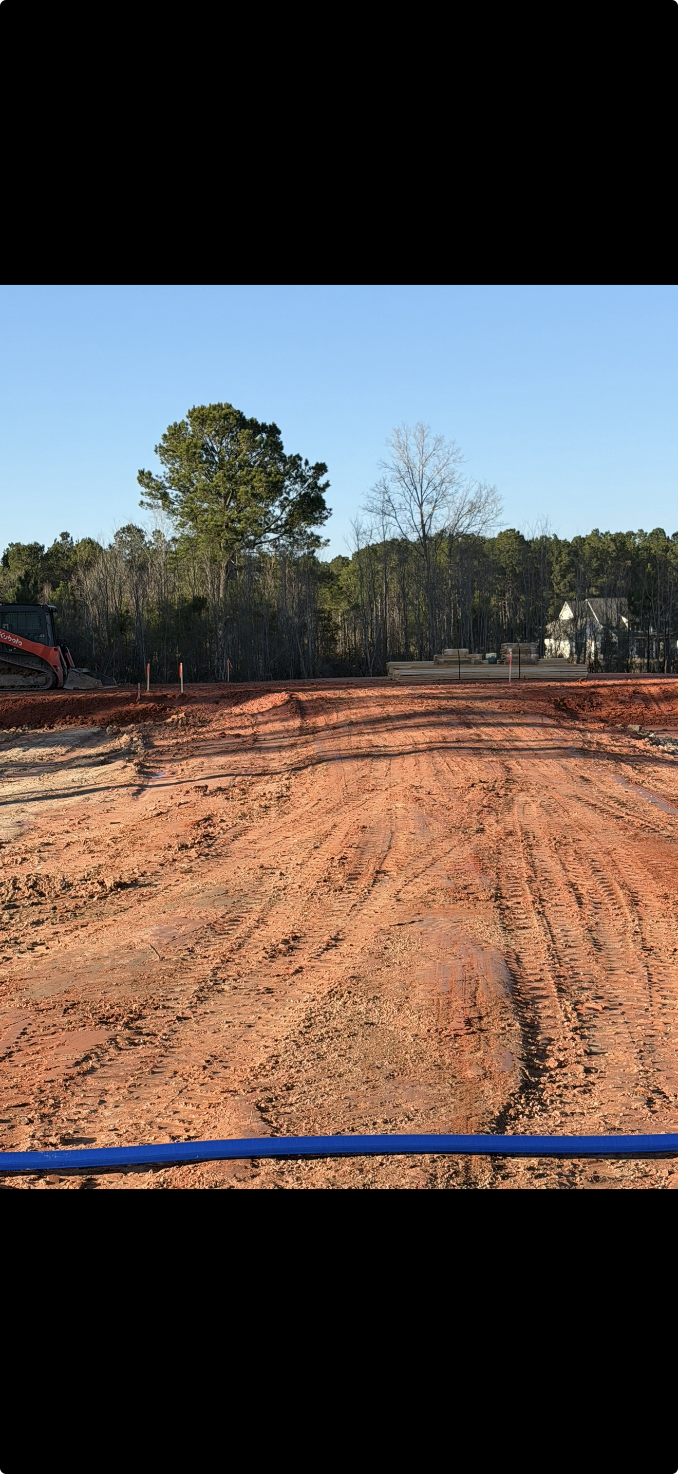 A garden bed under construction with a wooden frame filled with gravel in a backyard, surrounded by green grass, bushes, and trees.