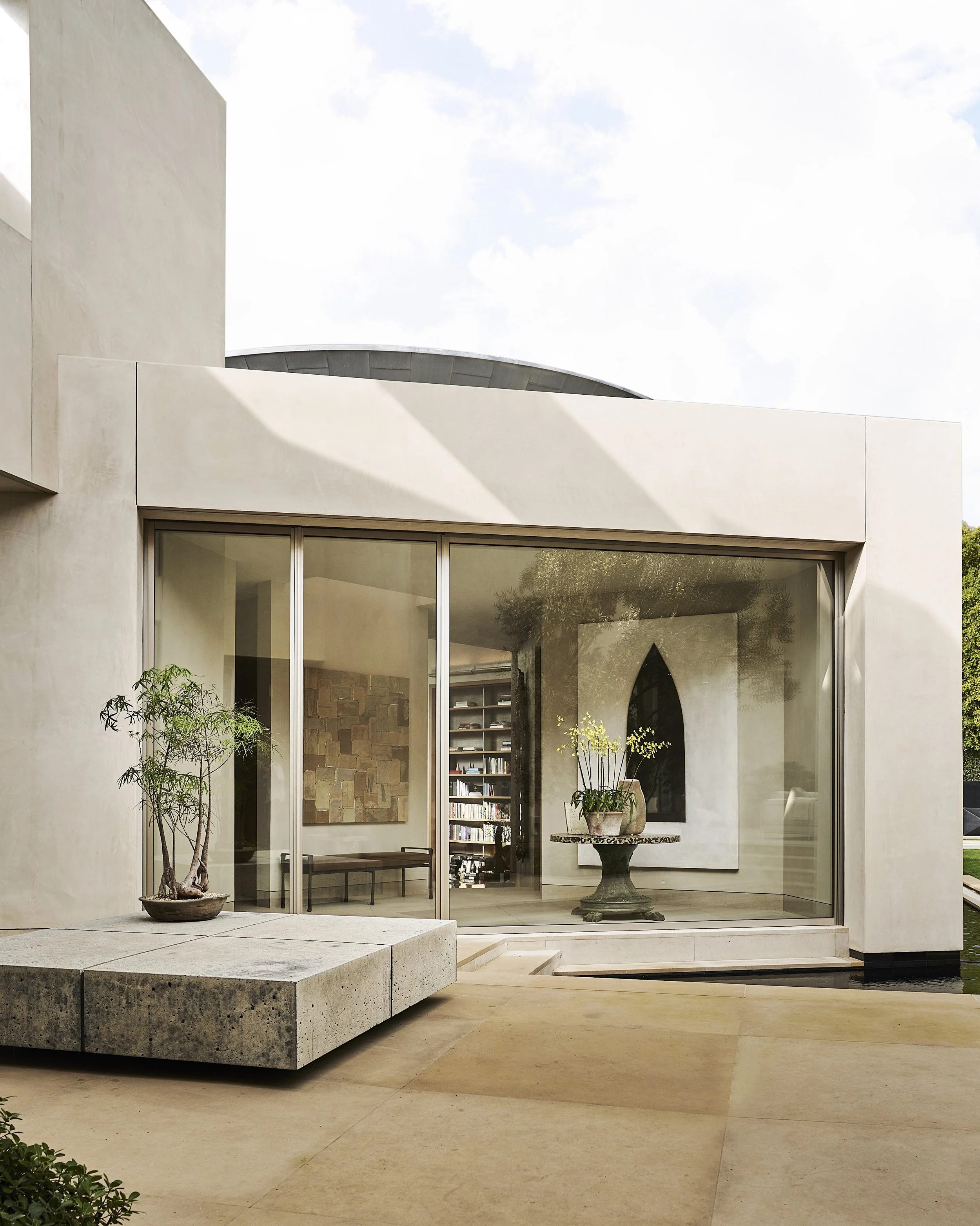 Modern house with large glass sliding doors, a potted plant outside, and an interior featuring art, a bookshelf, and decorative items.