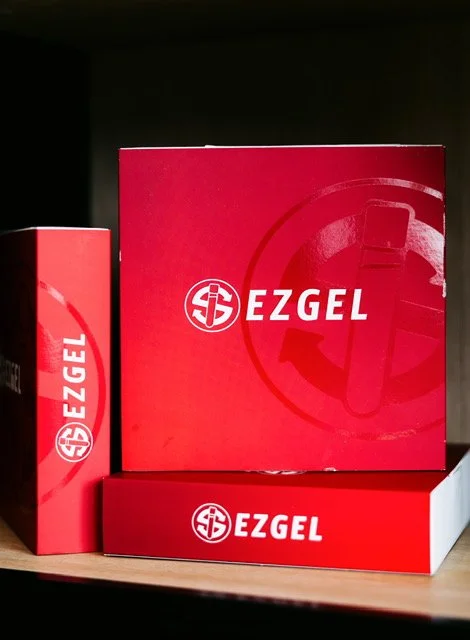 Three boxes of EZGEL products, with a large red box and two smaller boxes, arranged on a shelf.